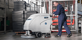 A worker uses an industrial floor sweeper to clean the floor of a facility