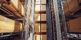 Automated vertical storage system moving stacked cardboard boxes inside a high-density warehouse facility.