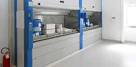 A blue vertical reciprocating conveyor holding various warehouse items along a warehouse wall