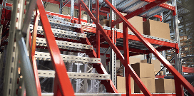 A red mezzanine shelf holds multiple levels of packages and features a set of steps for easy access
