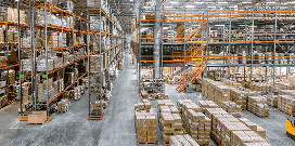 Rows of orange mezzanine shelves are accessed by catwalks in front of stacks of packages in a warehouse facility