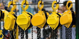A row of yellow below-hook lifting devices with black chains hanging in a facility
