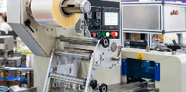 Industrial packaging machine wrapping products in plastic film inside a manufacturing facility.