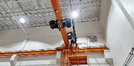 Technician performing maintenance on an overhead crane system using an elevated platform inside an industrial facility.