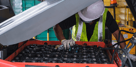Worker in safety gear inspecting and maintaining industrial batteries inside warehouse equipment.
