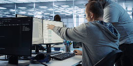 Two colleagues collaborating at a workstation, reviewing code and data on multiple monitors in a modern office.