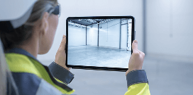 Worker holds a tablet while photographing the empty floor space of a building