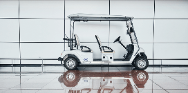 A white electric utility vehicle parked in front of a white wall on a reflective surface