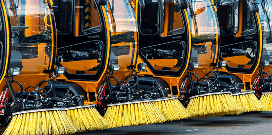 A row of orange floor sweeper equipment with yellow brushes
