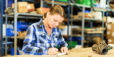 A worker writes notes about an auto part on a table in a warehouse facility
